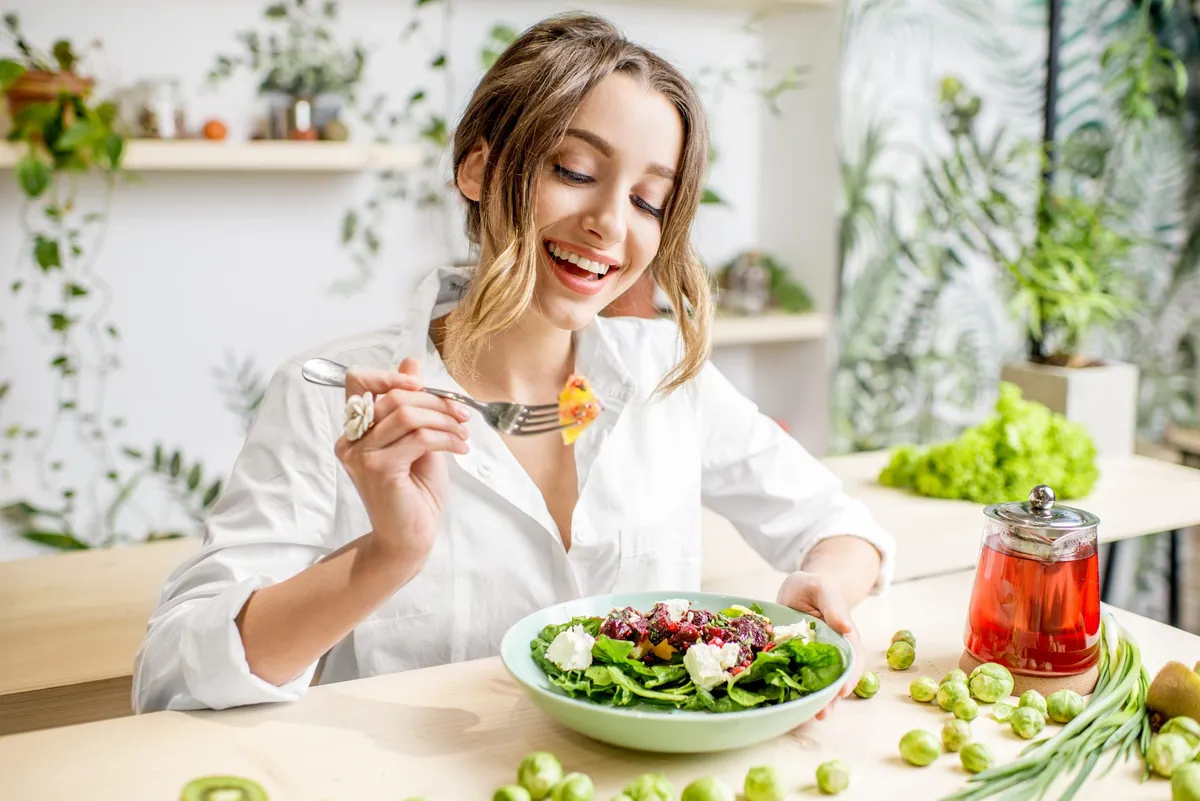 Femeie care mănâncă o salată verde lângă ceai de fructe, pentru imunitate